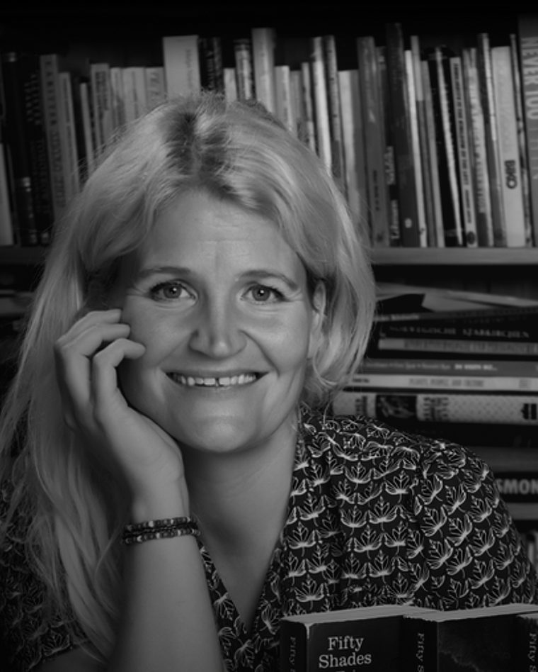 Liv Gulbrandsen lener hodet mot hånden foran en full bokhylle. Svart-hvitt-portrett.